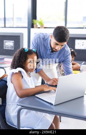 In school, Asian male teacher helping young biracial female student with a laptop in the classroom Stock Photo