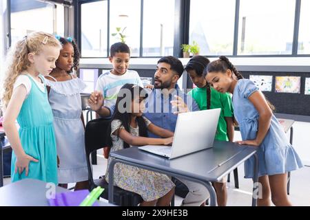 In school, young Asian male teacher and diverse students are looking at a laptop in the classroom Stock Photo