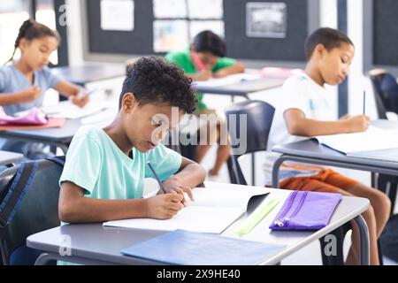 In school, group of biracial young students focusing on writing in the classroom Stock Photo