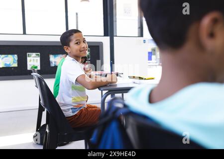 In school, two biracial boys are sitting at desks, looking at each other Stock Photo