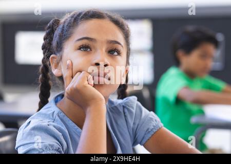 In school, young biracial female student thinking, another studying behind her Stock Photo