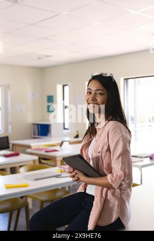Young biracial female teacher stands confidently in a classroom in high school. Her smile suggests a positive learning environment at school. Stock Photo
