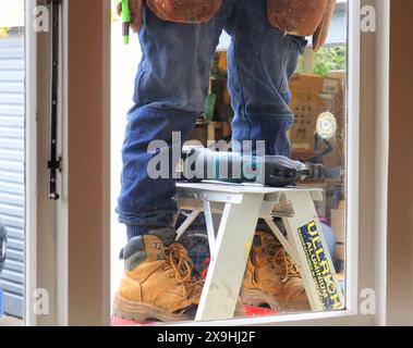 A builder stands astride a ladder outside the window of a house Stock Photo