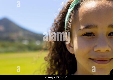 Biracial girl with curly hair smiles outdoors with copy space, green headband in her hair Stock Photo