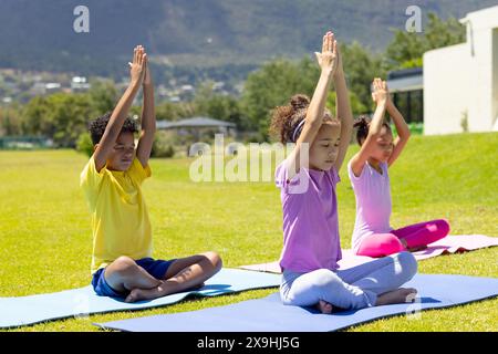 Biracial children practice yoga outdoors, sitting on colorful mats Stock Photo