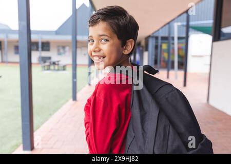 In school, young biracial male student wearing a backpack is smiling outdoors Stock Photo
