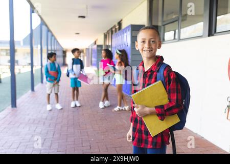 Biracial boy with a red plaid shirt and backpack smiles in a school corridor Stock Photo