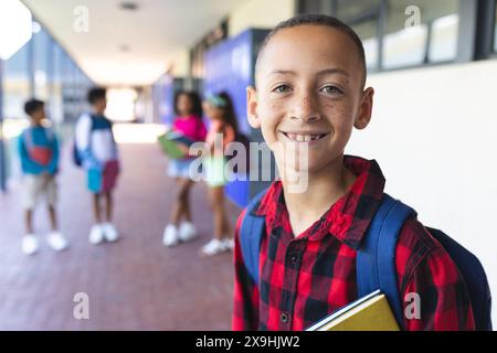 A biracial boy with a red plaid shirt and backpack smiles at school Stock Photo