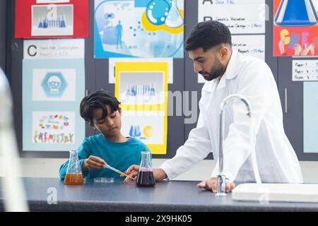 Young Asian male teacher assists biracial boy with a science experiment in school Stock Photo