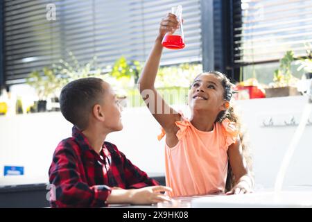 In school, biracial girl and boy are looking at red liquid in flask, doing a science experiment Stock Photo