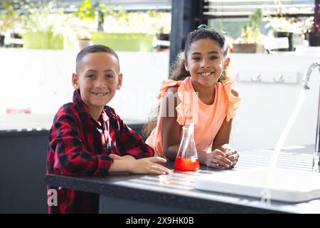 Biracial boy and girl engage in a science experiment at school, smiling at the camera Stock Photo
