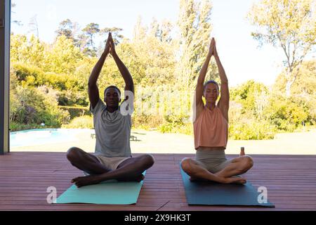 A diverse young couple practicing yoga outside beside pool Stock Photo