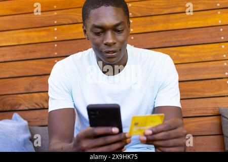 An African American young male holding credit card outside, browsing on a smartphone Stock Photo