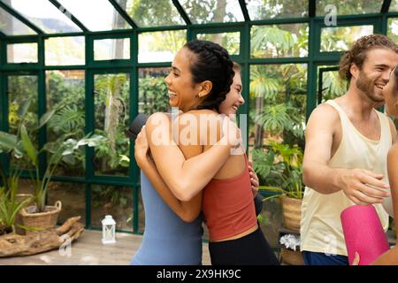 Diverse yoga students hugging in glass house studio Stock Photo