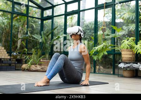Pacific Islander woman, yoga teacher in VR, sits on mat at Glass House Studio Stock Photo