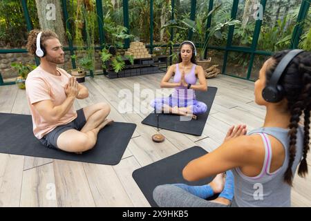 At Glass House Studio, diverse yoga students and instructor practicing in lush room Stock Photo