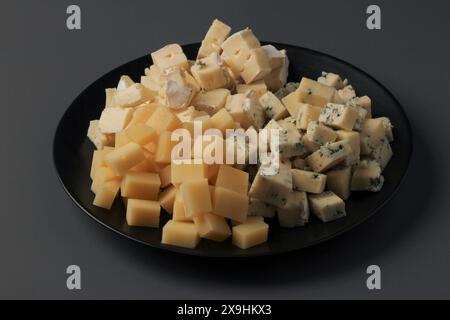 Sliced pieces of cheese assorted on a black dish on a gray background Stock Photo