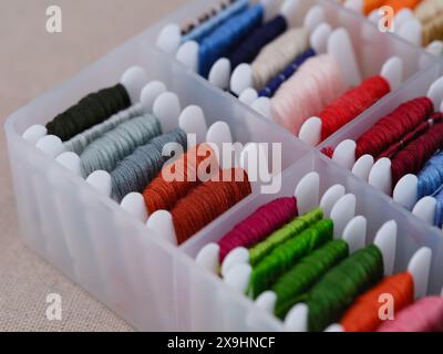 Plastic sorting box full of bobbins with different colour embroidery threads on a beige canvas background. Close-up Stock Photo