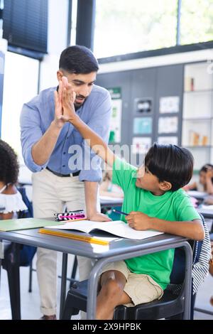 Young Asian male teacher gives a high-five to a biracial boy in a school classroom Stock Photo