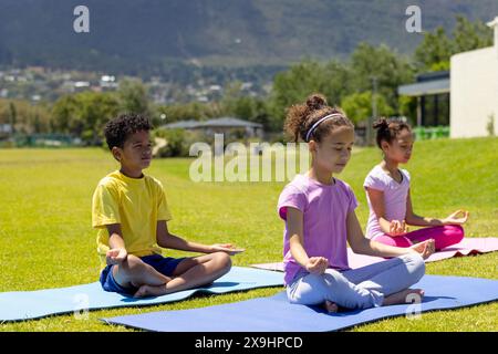 Biracial children practice yoga outdoors, with mountains in the background Stock Photo