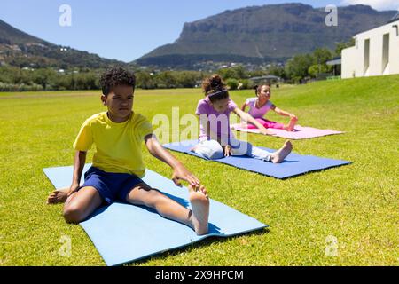 Biracial boy and girls practice yoga on mats in a sunny park Stock Photo