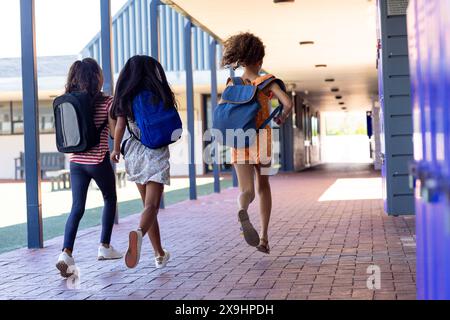 Three biracial girls with backpacks are walking down a school corridor Stock Photo