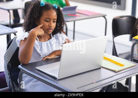 In school, young biracial female student is looking at a laptop in the classroom Stock Photo