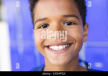 Biracial boy with a bright smile stands against a blue background in school Stock Photo