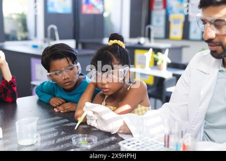 In school, Asian male teacher showing two biracial students science experiment Stock Photo