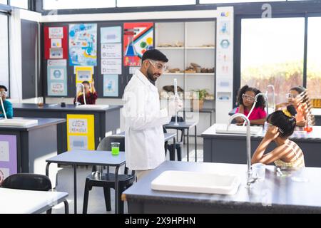 Asian male teacher with flask by diverse students in school science experiment Stock Photo