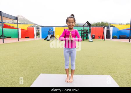 In school playground outdoors, a biracial young girl is practicing yoga Stock Photo