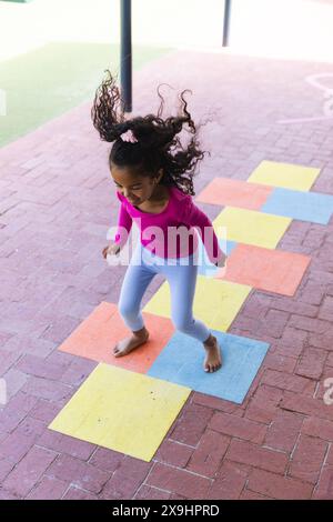 In school, young biracial girl is playing hopscotch alone outdoors Stock Photo