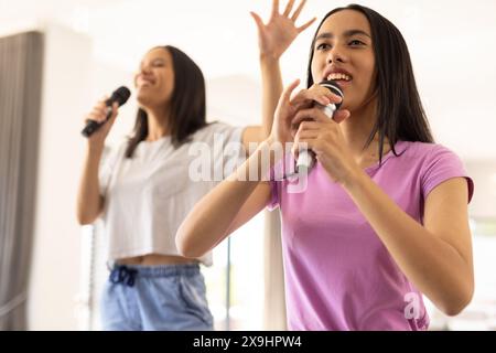 Two biracial young sisters, singing together at home, holding microphones Stock Photo