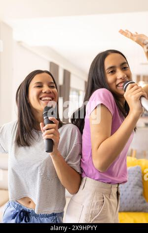 Two biracial young sisters, holding microphones at home, singing together Stock Photo