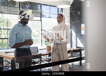 In modern business office, diverse team working together. African American male using VR headset, indian female holding documents, discussing ideas wr Stock Photo