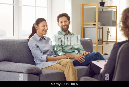 Happy husband and wife sitting on the couch and talking to their psychotherapist Stock Photo