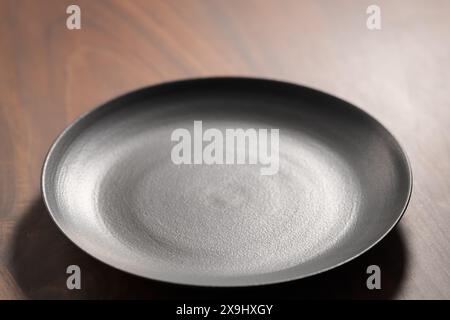 Empty black ceramic hand made plate on walnut wood table, shallow focus Stock Photo