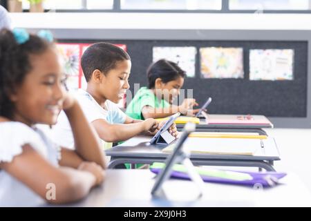 In school, diverse students using tablets and teacher monitoring in the classroom Stock Photo