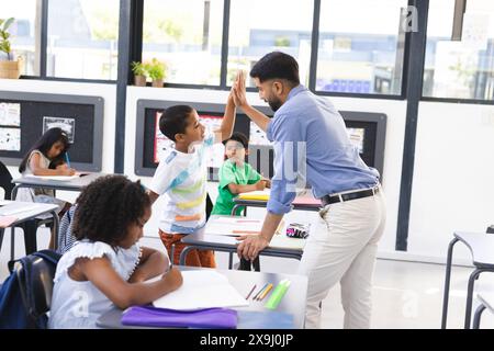 In school, young Asian male teacher giving high-five to a biracial male student in the classroom Stock Photo