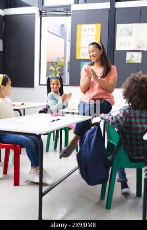 Biracial female teacher engaging with diverse students in classroom ...