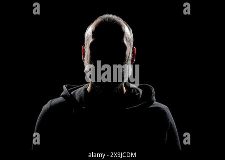 A silhouette of a bearded man in the dark with dramatic lighting to maintain anonymity. Stock Photo