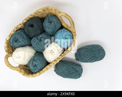 Flat lay photography of a turquoise, dark green, teal and white wool yarn balls in a basket on a white background Stock Photo