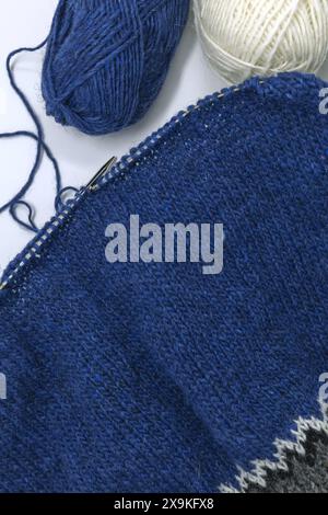 Flat lay photography of a blue wool yarn knitting on a metal needle with yarn balls on a white background, stockinette stitch knitted texture in progr Stock Photo