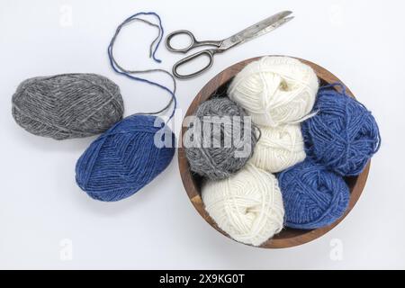 Flat lay photography of a blue grey white wool yarn balls in wooden basket and vintage scissors on a white background, stockinette stitch knitted text Stock Photo