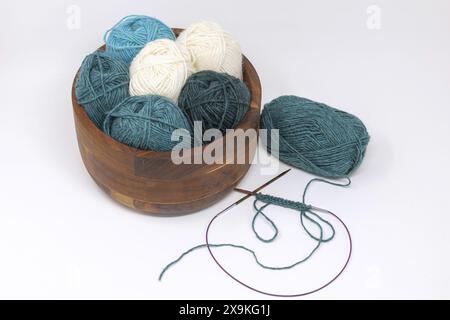 flat lay photography of a turquoise white wool yarn knitting on a wooden needles with yarn balls in a wooden basket on a white background Stock Photo