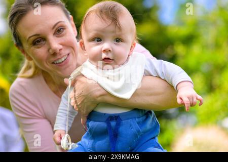 A happy mother, dressed in pink, holds her baby, who wears a white bib and blue pants. Stock Photo