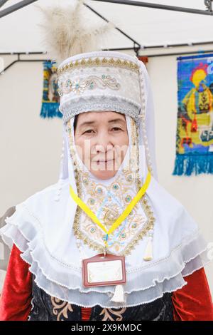 Almaty, Kazakhstan - March 20, 2024: Close-up portrait of senior Asian woman wearing traditional national Kazakh headdress with embroidery and feather Stock Photo