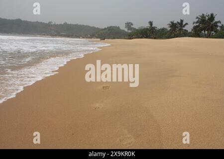 Close-up of footprints trailing along the edge of the shore, with gentle waves lapping at the sand. The footprints create a sense of solitude and refl Stock Photo