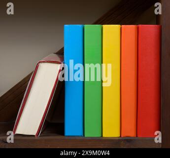 Horizontal shot of blank multicolored hardback books on a book shelf. One book is on its side. Stock Photo