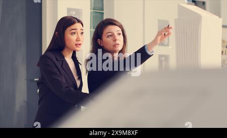 Industrial designers drawing lines on blueprints in agency office, examining 3d building maquette with sketches and outlines. Team of technician working at real estate small business, create drafts. Stock Photo